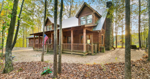 A rustic wooden cabin surrounded by trees, featuring a porch and an American flag, set in a serene natural landscape.