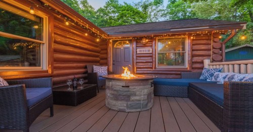 Cozy log cabin patio with a fire pit, seating, and string lights, surrounded by greenery. Perfect for relaxation.