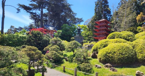 A serene garden with lush greenery, colorful flowers, and a traditional red pagoda under a clear blue sky.
