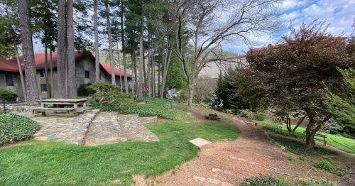 A serene outdoor scene featuring a stone path, lush greenery, and a rustic building surrounded by trees.