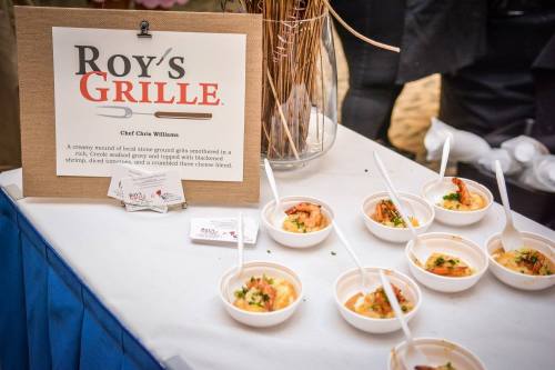 A table display featuring small bowls of shrimp and grits, with a sign for Roy's Grille and business cards.