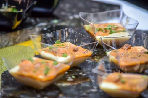 Small transparent cups filled with a creamy dish topped with herbs and chunks of meat, arranged on a dark surface.