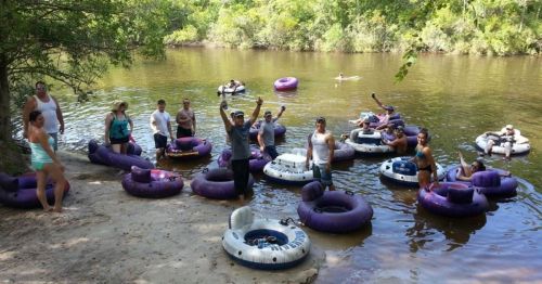 A group of people enjoying a river day, floating on inner tubes and relaxing by the water under a sunny sky.