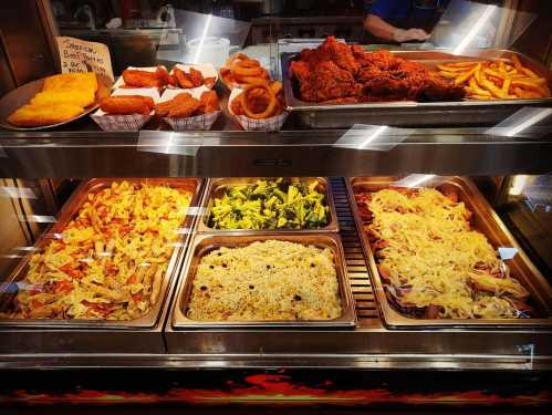 A display of various foods including fried chicken, onion rings, rice, broccoli, and pasta in a food service counter.