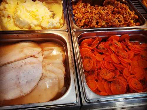 Four food trays featuring mashed potatoes, stuffing, sliced turkey, and seasoned carrots.