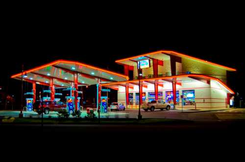 A brightly lit gas station at night, featuring multiple fuel pumps and a convenience store.