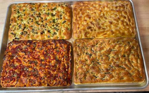 A tray of four types of baked focaccia, each with different toppings and colors, arranged in a grid pattern.