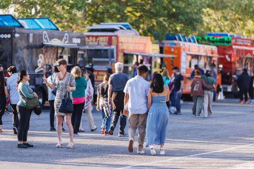 A busy food truck event with people walking, chatting, and enjoying various food options in a vibrant outdoor setting.