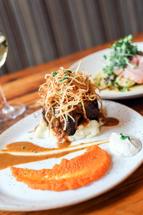 A plate of beef topped with crispy onions, served on mashed potatoes with sauce and a side of carrot puree.