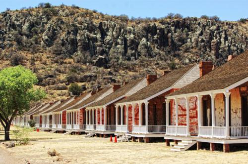 Row of historic buildings with porches, set against a rocky hillside and dry landscape.