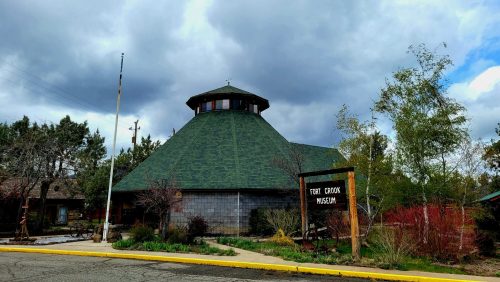 A round, green-roofed building with a sign reading "Fort Crook Museum," surrounded by trees and cloudy skies.