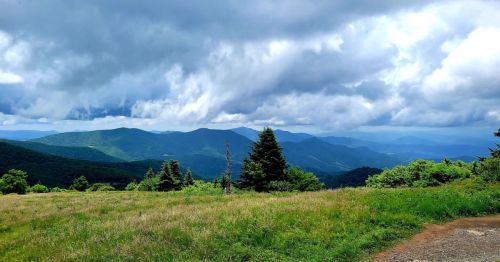 A scenic view of rolling green mountains under a cloudy sky, with a grassy foreground and distant peaks.