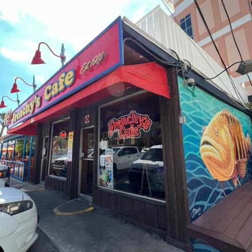 Exterior of Frenchy's Cafe featuring a colorful mural of a fish and red awnings, with parked cars nearby.