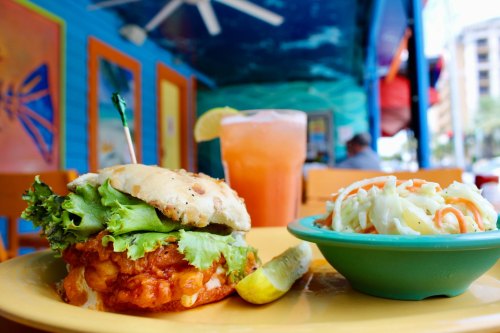 A vibrant plate featuring a spicy chicken sandwich with lettuce, a side of coleslaw, and a colorful drink.