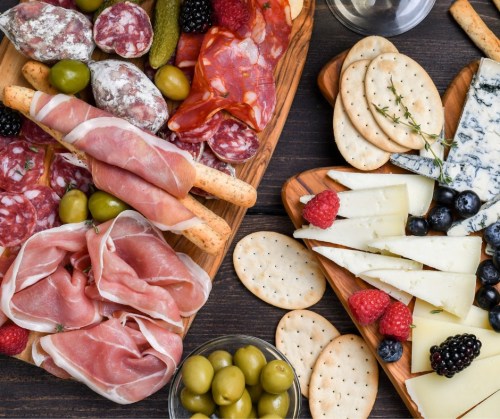 A wooden platter with assorted meats, cheeses, olives, crackers, and fresh berries arranged artfully.