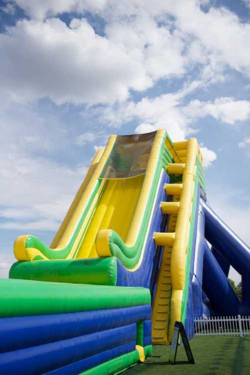 A large inflatable water slide in bright blue and yellow, set against a cloudy sky.