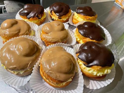 A tray of cream-filled pastries topped with chocolate and caramel icing, arranged on paper liners.