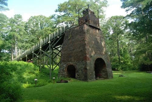 Historic brick structure surrounded by greenery, featuring a tall chimney and wooden platform above.