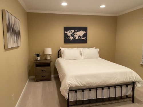 Cozy bedroom featuring a bed, nightstand, lamp, and wall art with a world map on a warm-toned wall.
