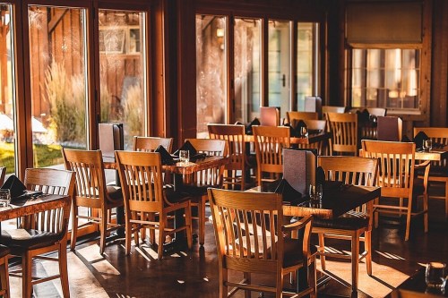 Cozy restaurant interior with wooden tables and chairs, bathed in warm sunlight through large windows.