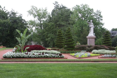 A landscaped garden featuring colorful flowers, neatly trimmed shrubs, and a statue surrounded by greenery.