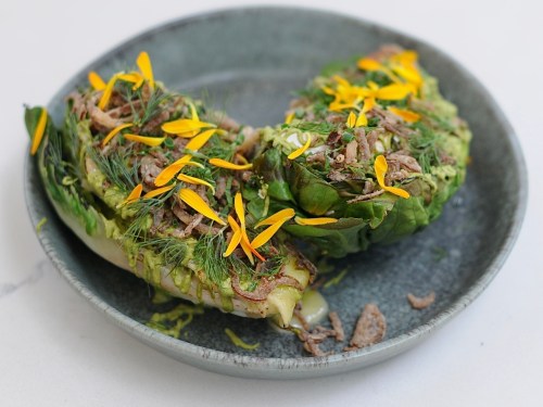 Grilled lettuce halves topped with herbs, crispy shallots, and vibrant edible flowers on a gray plate.