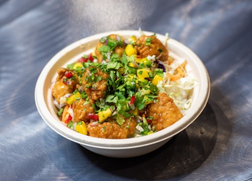 A bowl of crispy chicken topped with mango salsa and fresh herbs, served on a bed of shredded cabbage.