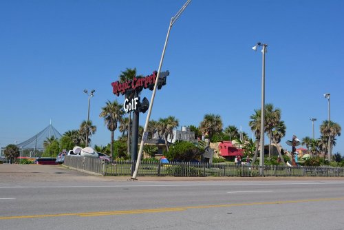 A colorful mini-golf course with palm trees and whimsical structures, featuring a leaning sign and clear blue sky.