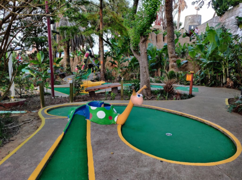A colorful mini-golf course featuring a whimsical snail sculpture amidst lush greenery and tropical plants.