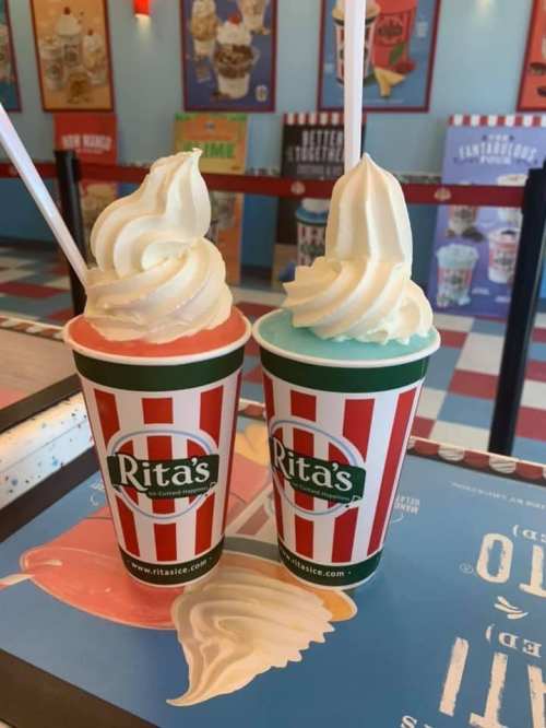 Two colorful cups of frozen treats from Rita's, one with red and white stripes and the other green and white, topped with soft serve.