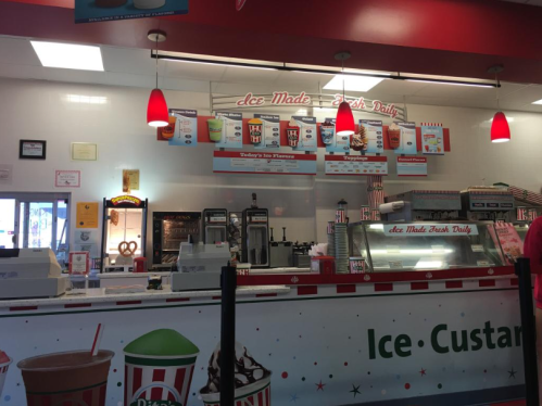 A colorful ice cream shop counter with various ice cream flavors, toppings, and a menu displayed above.