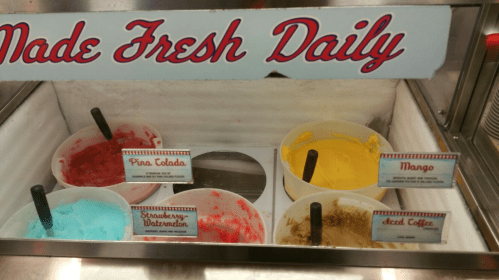 Ice cream display with six flavors: Pina Colada, Strawberry-Watermelon, Mango, Decaf Coffee, and more, labeled and colorful.
