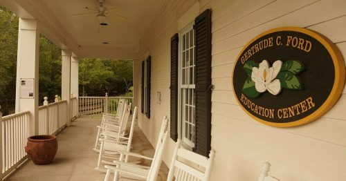 Porch of the Gertrude C. Ford Education Center with rocking chairs and a decorative sign featuring a magnolia.