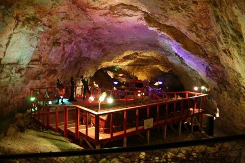 A colorful underground cave with a wooden platform and figures silhouetted against the illuminated rock walls.