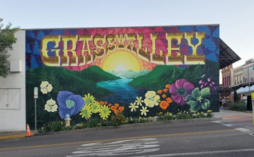 Colorful mural featuring "Grass Valley" with flowers and a sunset over a river and mountains.