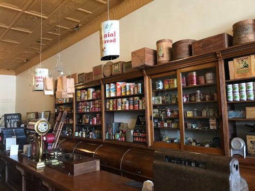 Interior of a vintage general store with wooden shelves filled with canned goods and old-fashioned decor.