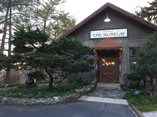 A rustic building with a sign reading "Antique Car Museum," surrounded by trees and decorative lights.