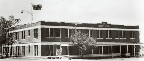 Black and white photo of the Mobley Hotel, a two-story brick building with a sign and trees in front.
