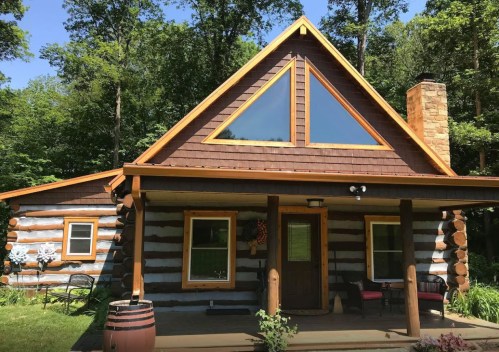 A charming log cabin with a triangular window, surrounded by trees and featuring a welcoming porch.