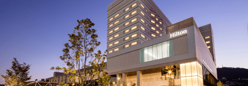 Exterior view of a Hilton hotel at dusk, featuring modern architecture and illuminated windows.