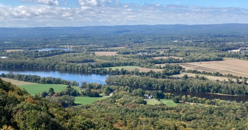 A scenic view of rolling hills, a river, and farmland under a partly cloudy sky.