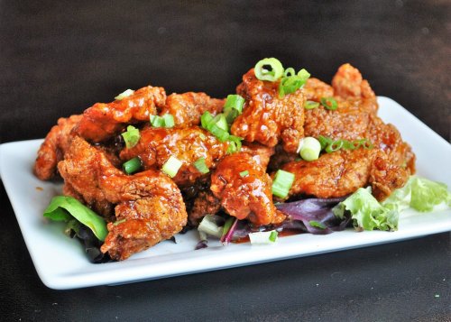 A plate of crispy fried chicken coated in a glossy sauce, garnished with green onions, served on a bed of lettuce.
