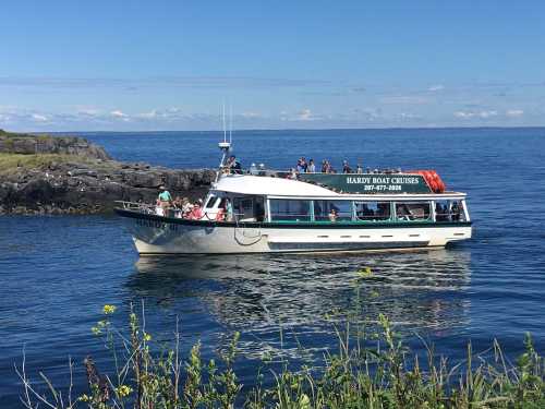 A tour boat named "Hardy II" with passengers on board, floating on calm blue waters near rocky shores.