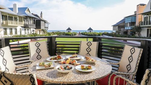 A beautifully set outdoor dining table with various dishes, overlooking a scenic view of the ocean and nearby buildings.