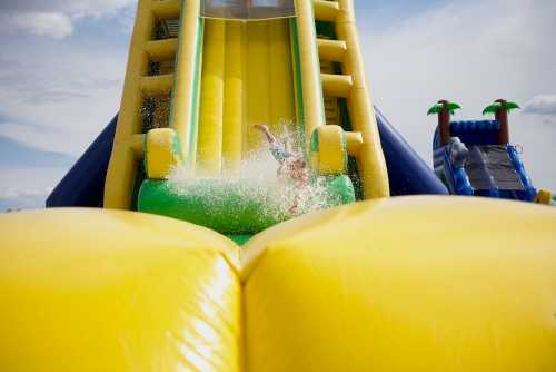 A child splashes into a pool at the bottom of a colorful inflatable water slide on a sunny day.