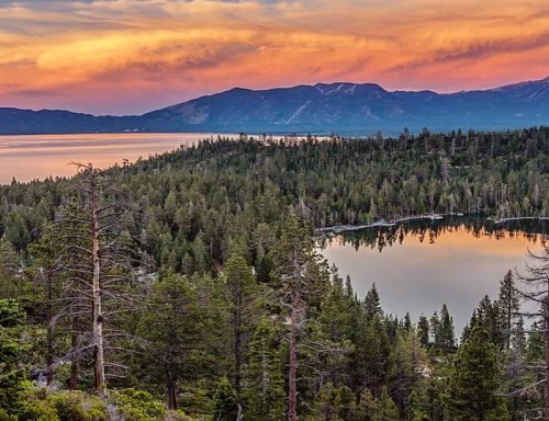 A serene landscape featuring a lake surrounded by lush forests and mountains, under a colorful sunset sky.