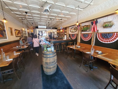 A cozy restaurant interior with wooden tables, a barrel, and patriotic decorations, featuring a warm, inviting atmosphere.