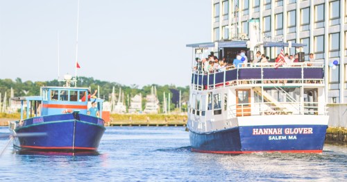 Two boats in a harbor: a blue fishing boat and a larger passenger boat named "Hannah Glover" in Salem, MA.