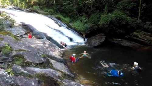 People enjoying a natural waterfall and swimming in a rocky pool surrounded by lush greenery.