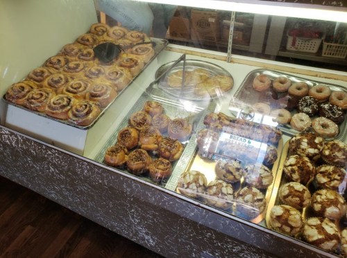 A display case filled with various baked goods, including cinnamon rolls, pastries, and donuts.